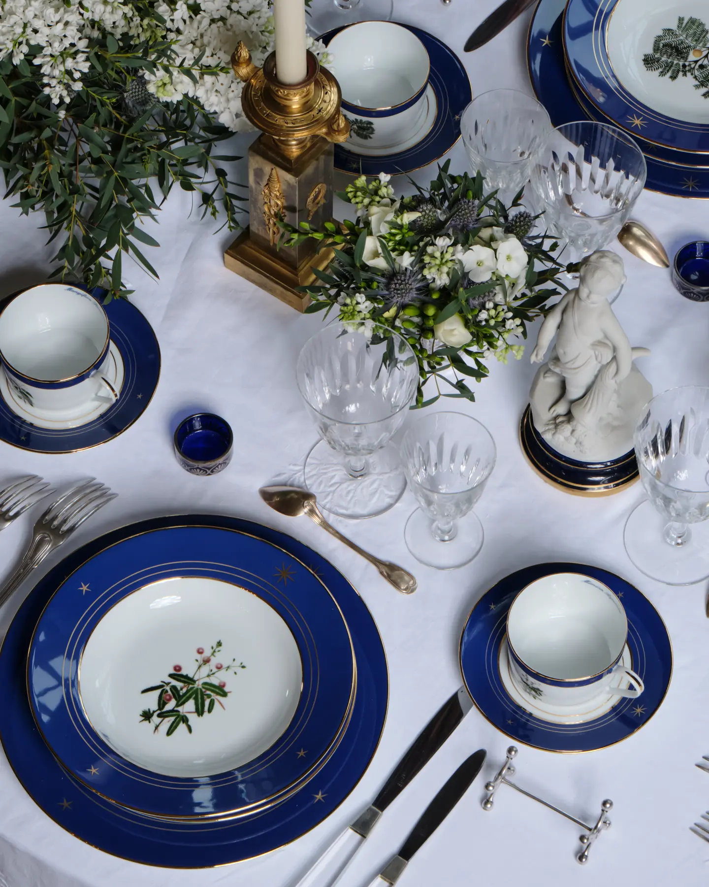 Elegant blue-gold table setting with floral centerpiece and crystal glassware on a white tablecloth