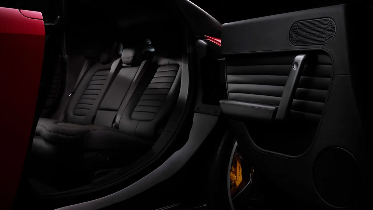Open car door reveals a sleek interior with black leather seats in a sports car and a yellow brake caliper visible behind the wheel.