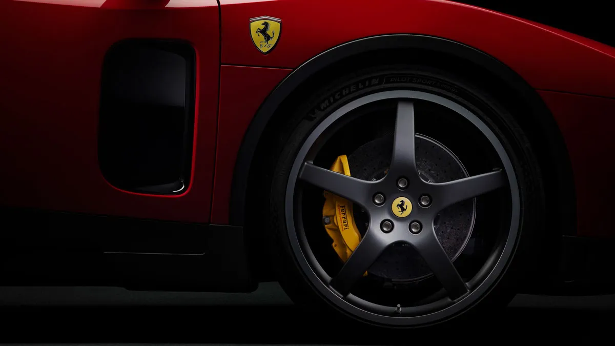 Close-up of a red Ferrari wheel: five-spoke rim, yellow brake caliper, and Ferrari emblem visible on the bodywork.