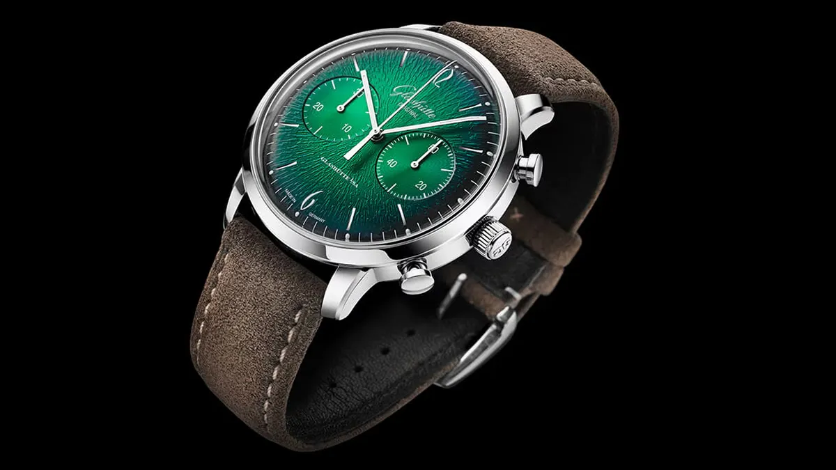 Green dial wristwatch with brown suede strap and silver case photographed on black background, close-up detail included crown and pushers.