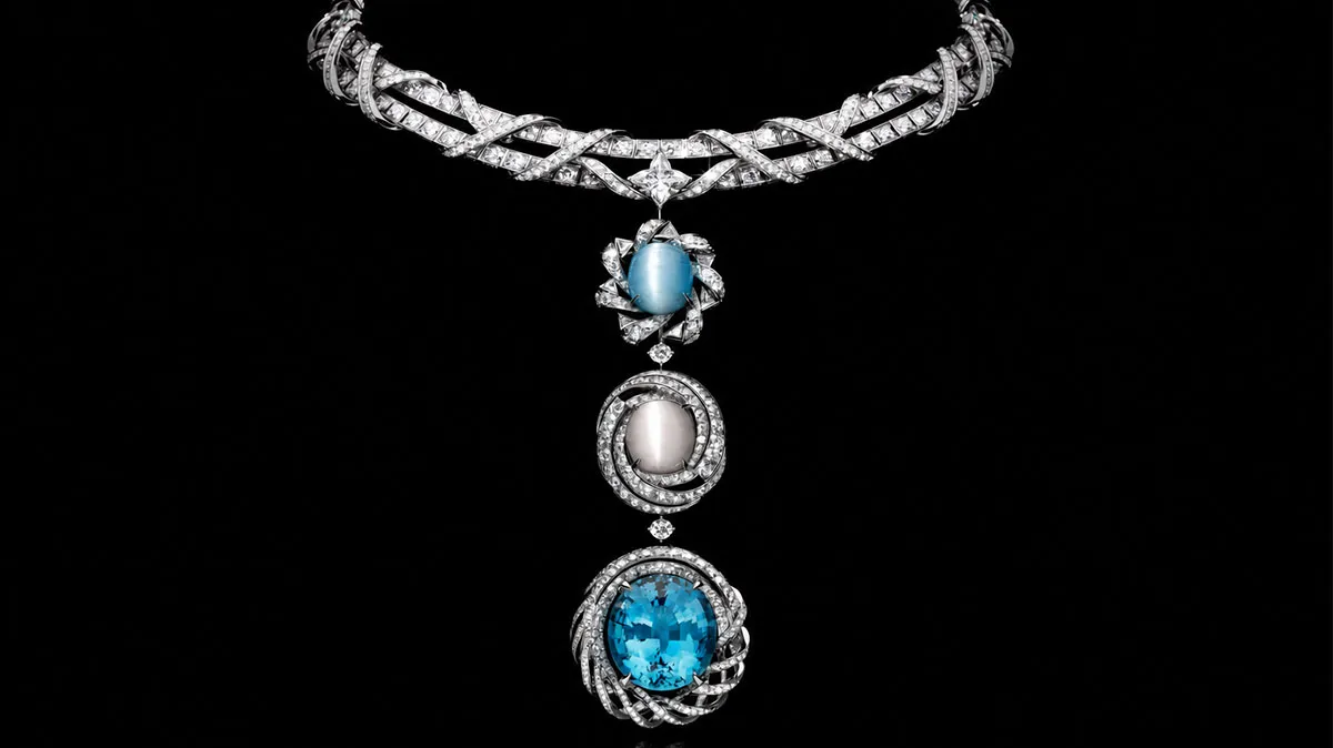 Diamond necklace featuring a multi-gemstone pendant: blue cabochon, pearl-like bead, and a large blue gemstone in intricate diamond settings on a black background