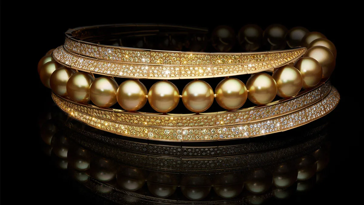 Gold bracelet set with lustrous pearls and pavé diamonds on a black reflective surface, elegant jewelry display