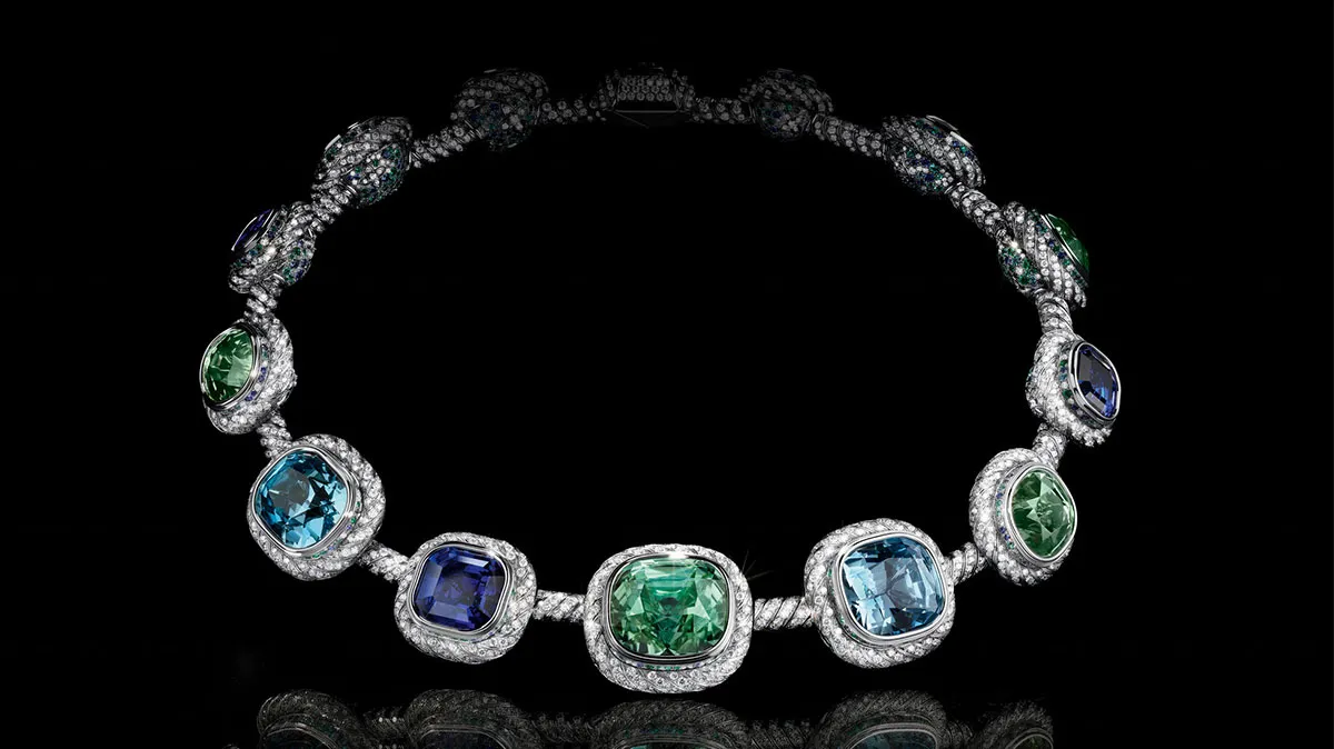 Diamond-studded necklace with alternating emeralds and sapphires set in pavé-diamond halos on a black background, showcasing blue and green stones.