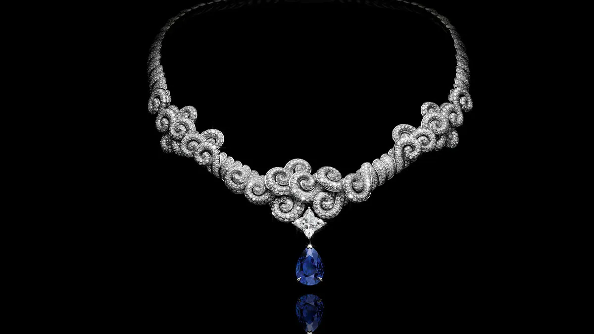 Diamond necklace with intricate looped pavé design and a blue teardrop pendant against a black background.