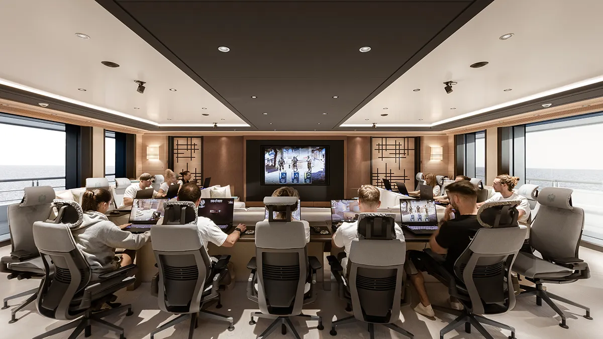Group of people gaming in a modern, ocean-view conference room with laptops, facing a large central screen.