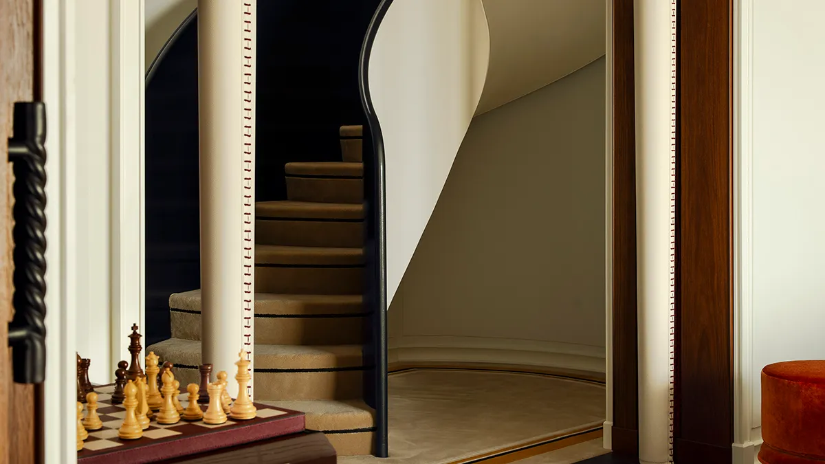 Interior with a curved staircase visible through an open doorway, and a chessboard with wooden pieces on a table to the left.