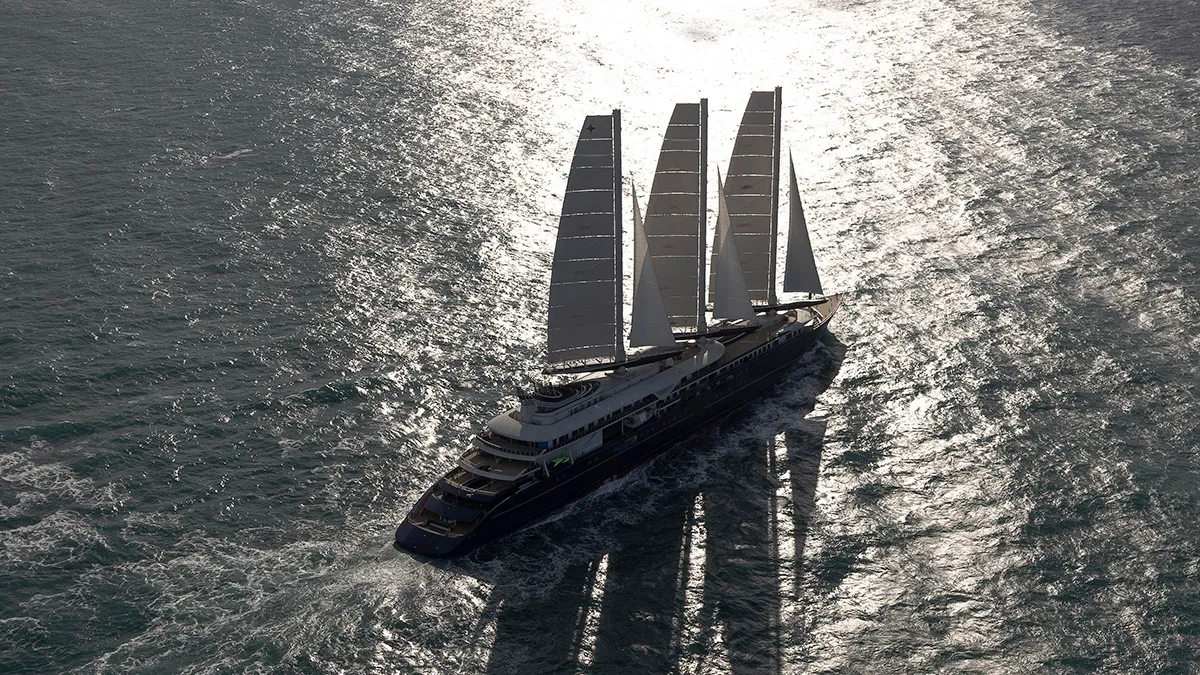 Aerial view of a four-masted luxury sailing yacht cutting through sunlit ocean.