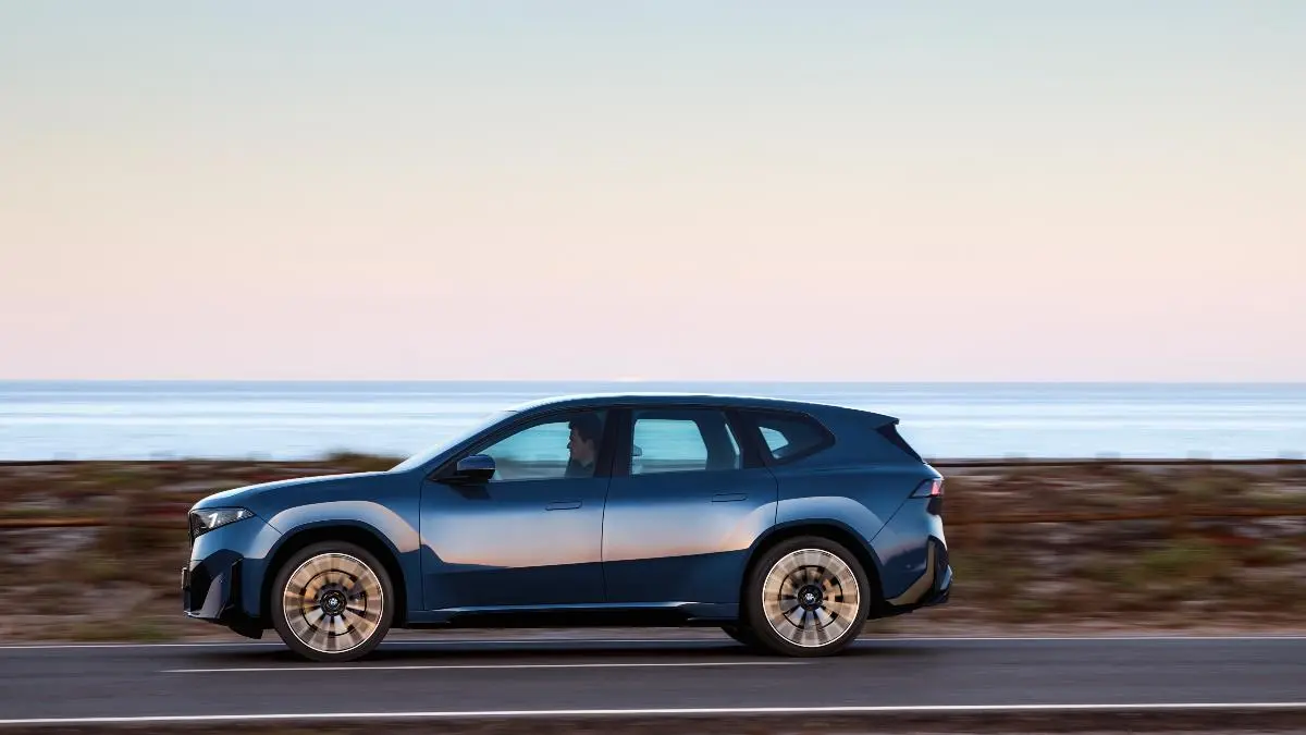 Blue SUV driving along a coastal highway at sunset with the ocean in the background, in motion.