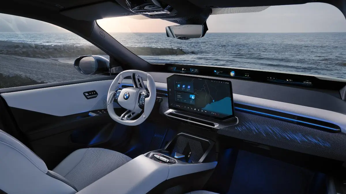 BMW interior with white steering wheel and a large central touchscreen, ocean view outside the windows, blue ambient lighting.