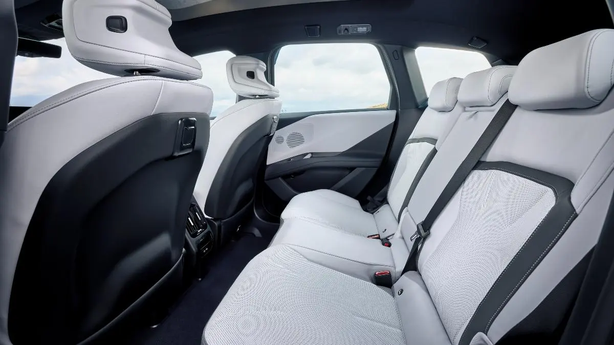 Rear passenger cabin of a modern car with light gray perforated seats and headrests, black door panels, and rear air vents nearby.