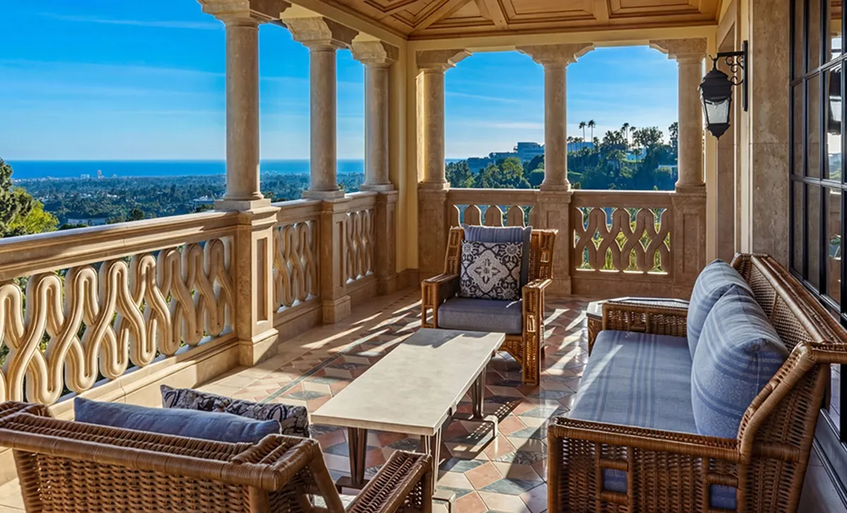 Balcony seating area with wicker chairs and a sofa, overlooking a city and blue ocean under a sunny sky.
