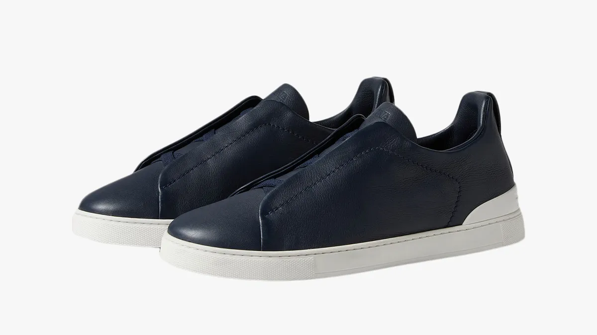 Navy blue slip-on sneakers with white rubber sole viewed from side, casual footwear for men or women