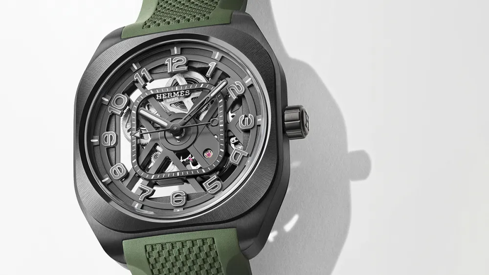 Skeleton-dial wristwatch with exposed gears, gray case, and green textured strap.