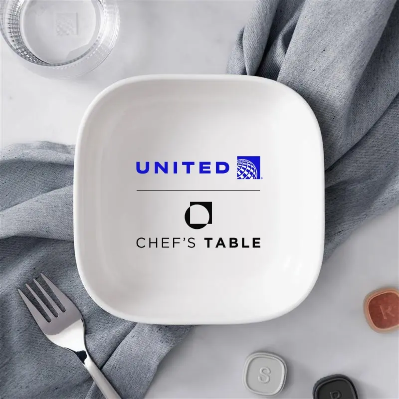 White square plate showing United Airlines logo and the text 'Chef's Table', with a gray napkin and fork nearby for a dining promo image.