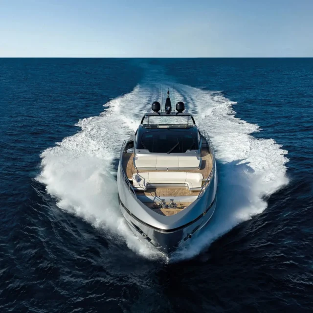 Luxury motor yacht cruising on blue sea with wake; circular inset shows a man in a red Ferrari polo shirt with sunglasses hanging from his chest.