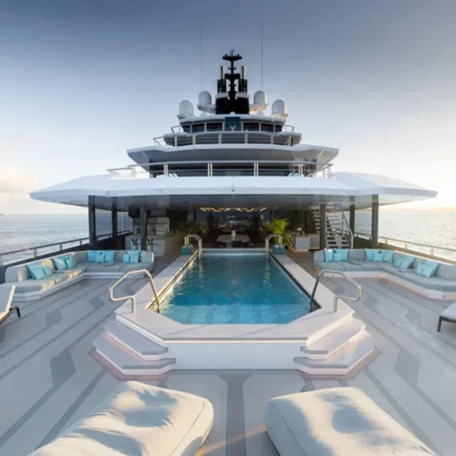Luxury yacht deck with a central pool, white loungers, and a sunset over the sea.