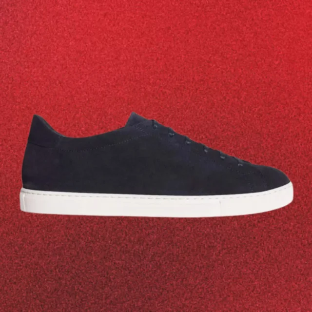 Three sneakers in white, black, and beige float against an orange background, arranged diagonally from top left to bottom right used as a fashion hero image.
