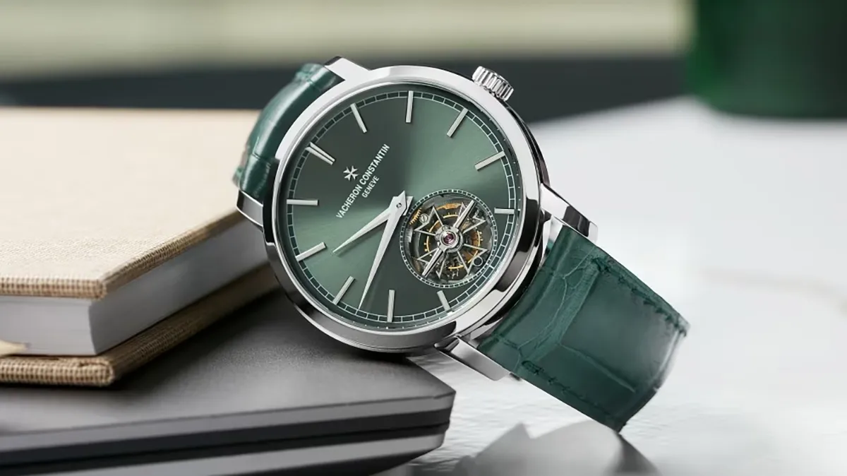 Green-dial luxury wristwatch with a tourbillon, silver case, and green leather strap resting on notebooks.