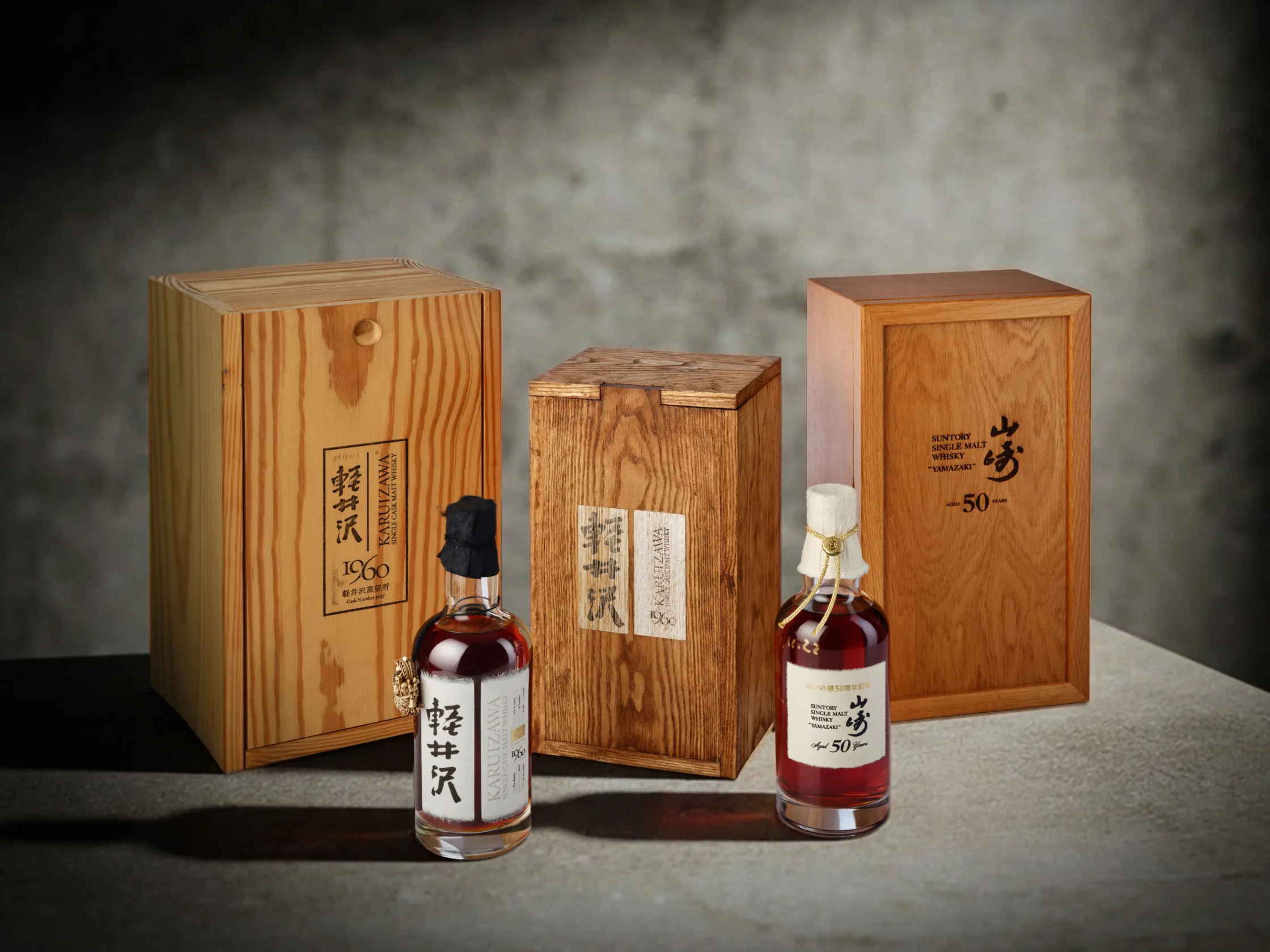 Three wooden whiskey boxes with two bottles in front, set against a dark backdrop. One bottle labeled in Japanese rests on the left, a larger bottle on the right.