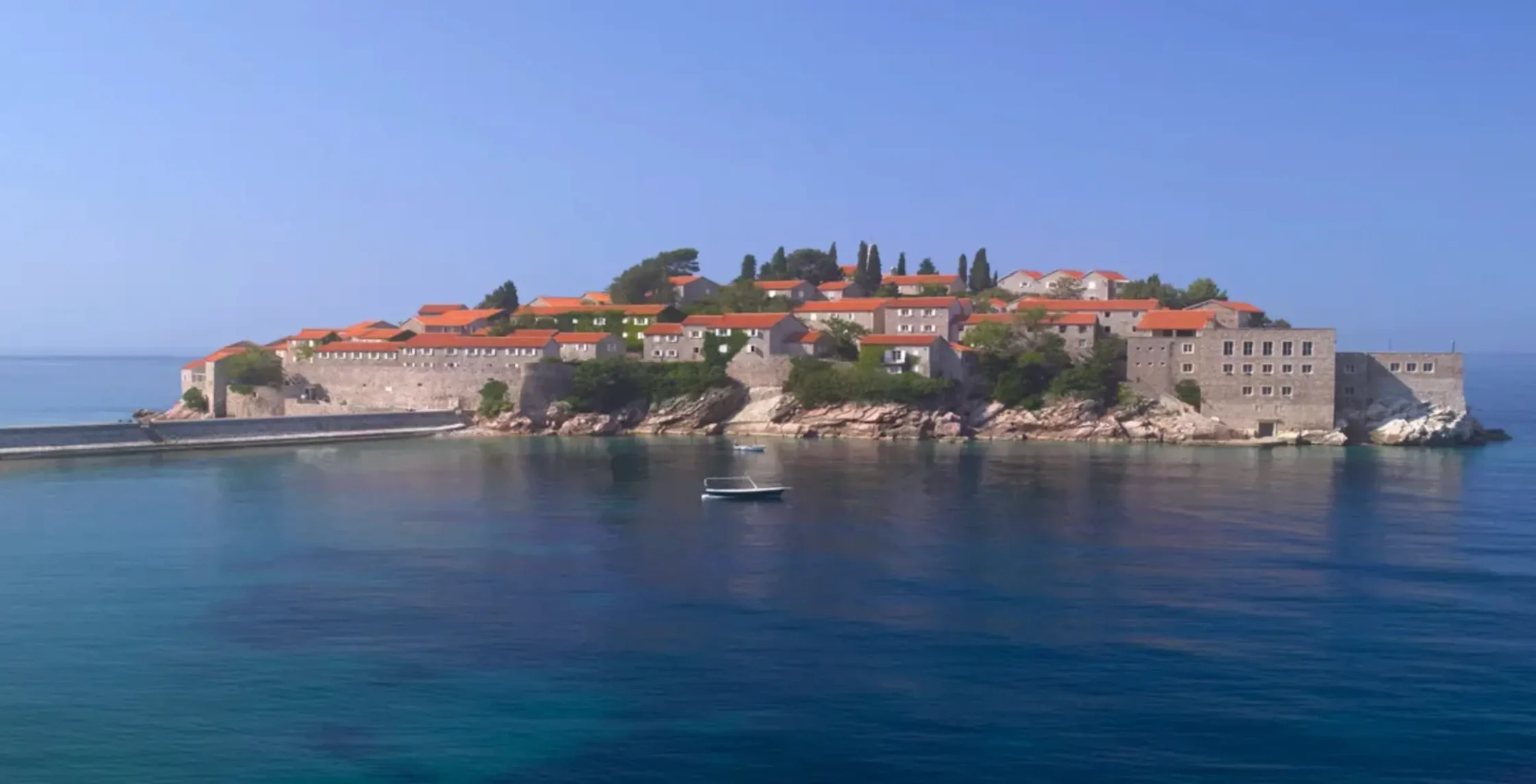Fortified island town with red-tiled roofs atop stone walls overlooking calm blue sea.