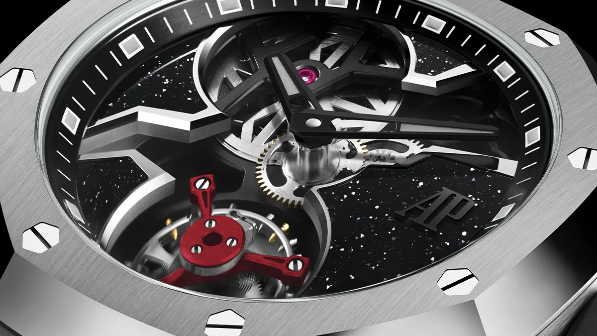 Close-up of a skeleton luxury watch showing gears, a red balance wheel, and a brushed metal case with the AP logo visible at the dial edge.