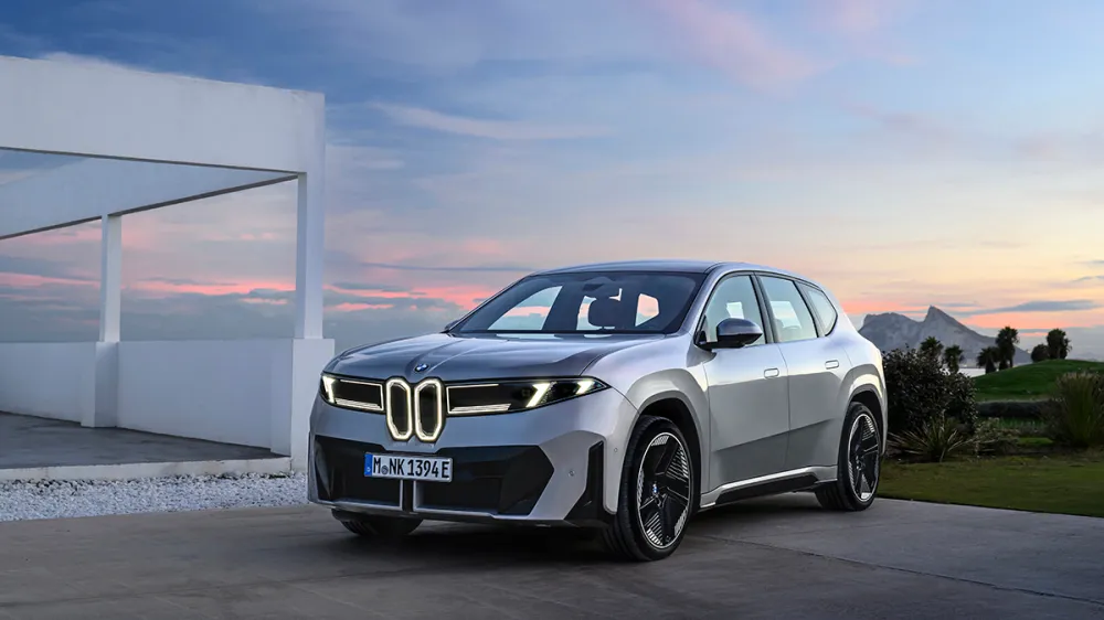 Silver BMW SUV parked on a driveway at sunset with a white modern building in the background.