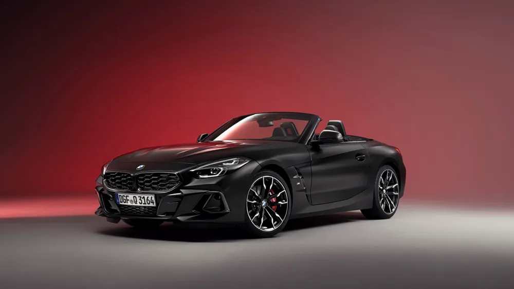 Black BMW convertible sports car in a studio with a red gradient background, front three-quarter view with the top down.