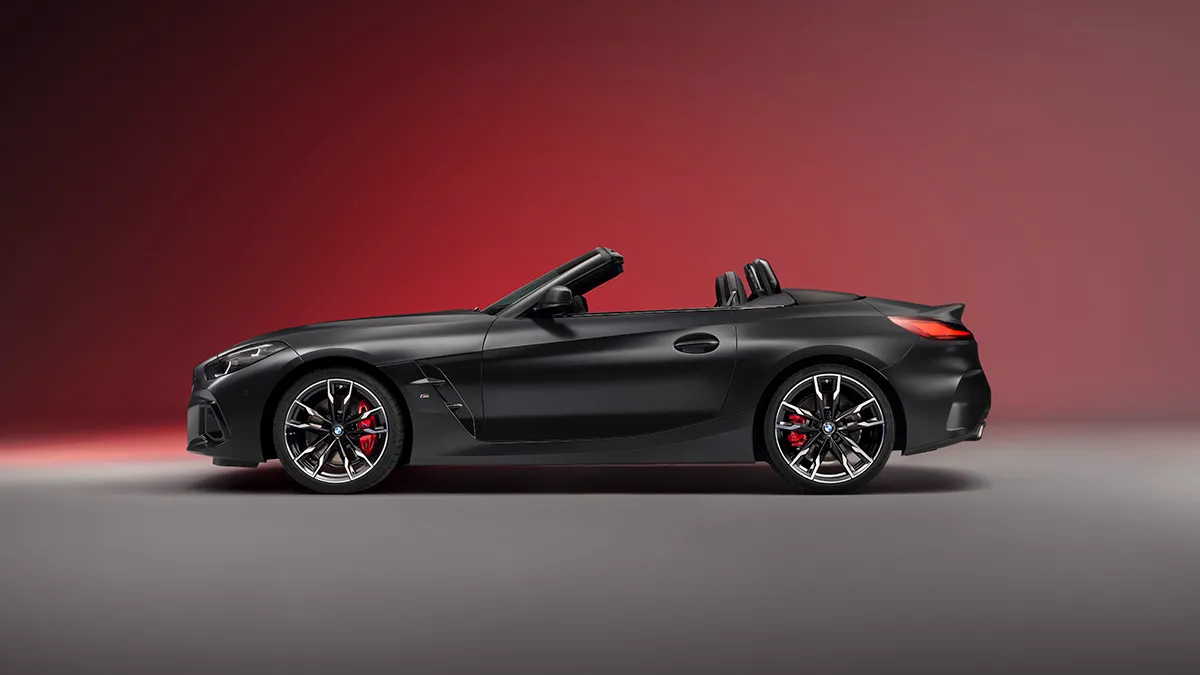 Side view of a black BMW convertible sports car with the top down, red brake calipers, and alloy wheels against a red gradient backdrop.