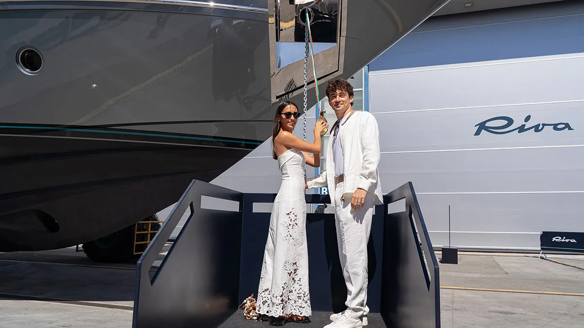 Couple dressed in white posing on a boarding ramp beside a large luxury yacht named Riva