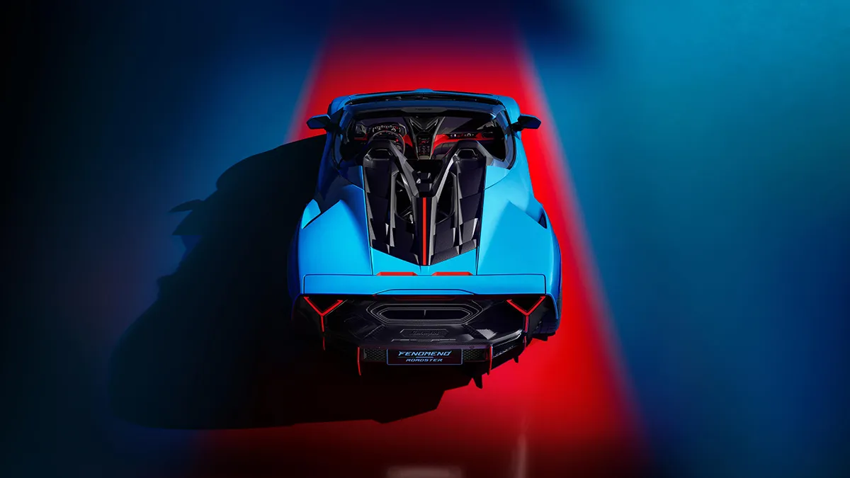 Exotic blue sports car viewed from above with open cockpit and red taillight accents in a dark studio setting
