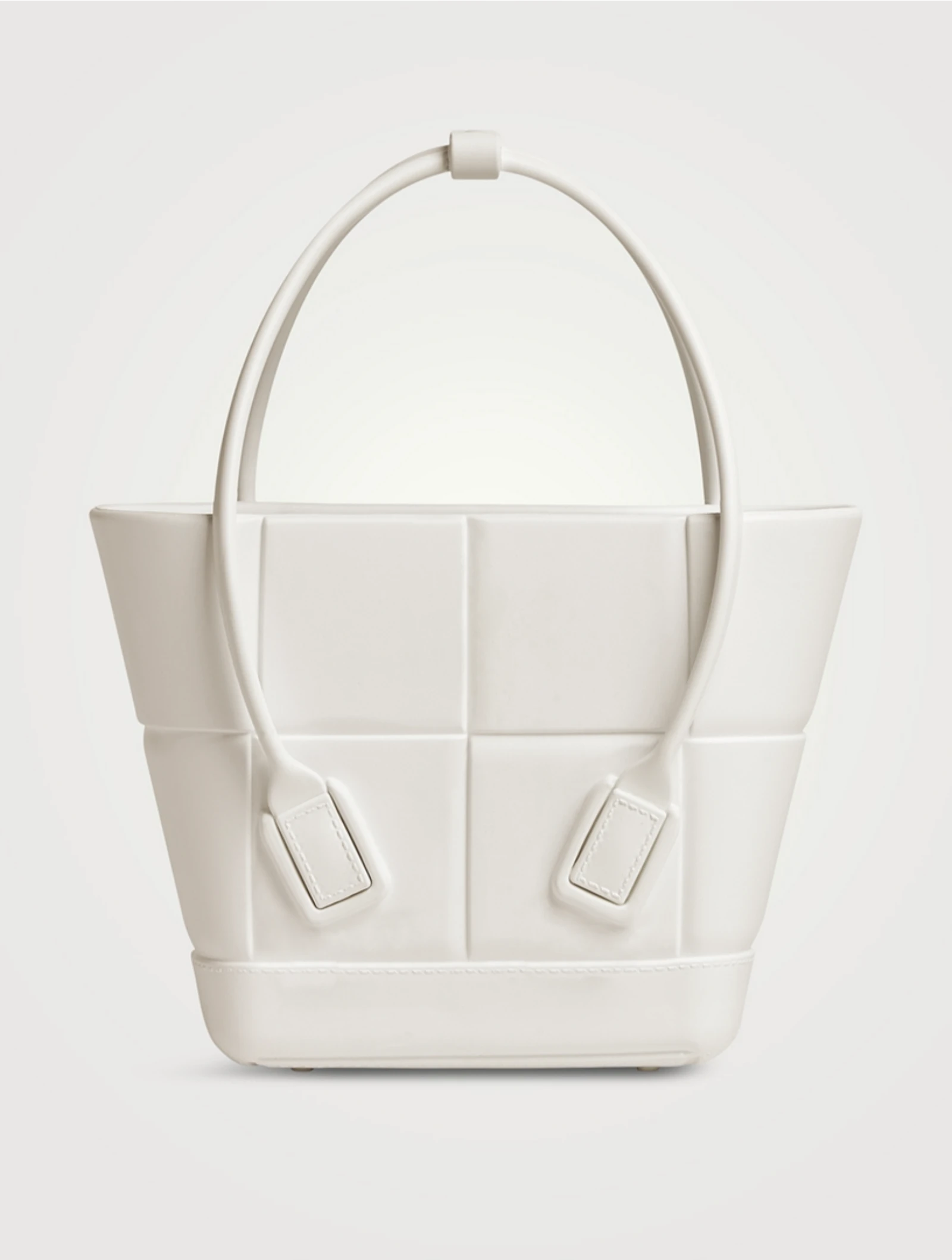 Close-up view of a white handbag with a curved handle and stitched straps, focusing on the bottom half of the bag