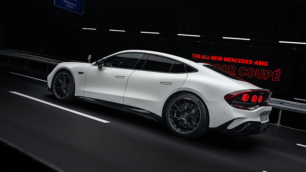 White Mercedes-AMG four-door coupe on a dark track, with black wheels and red taillights, and a red promo banner in the background.