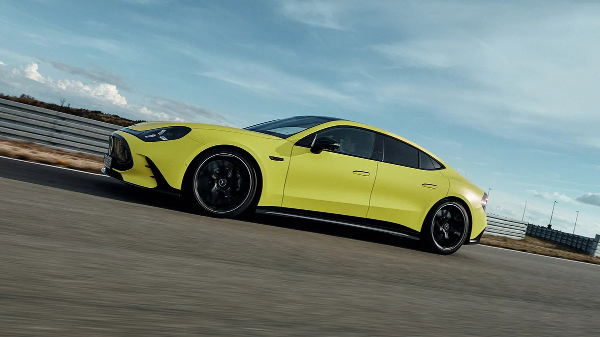 Bright yellow sports car speeding on a racetrack under a blue sky, side view.