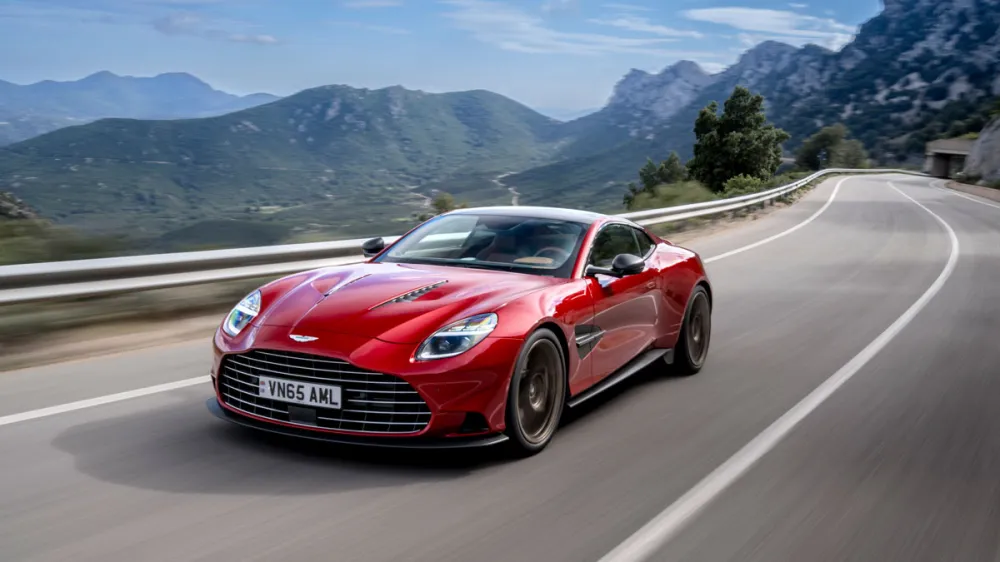 Red sports car driving along a curving mountain road with guardrails and distant hills in the background