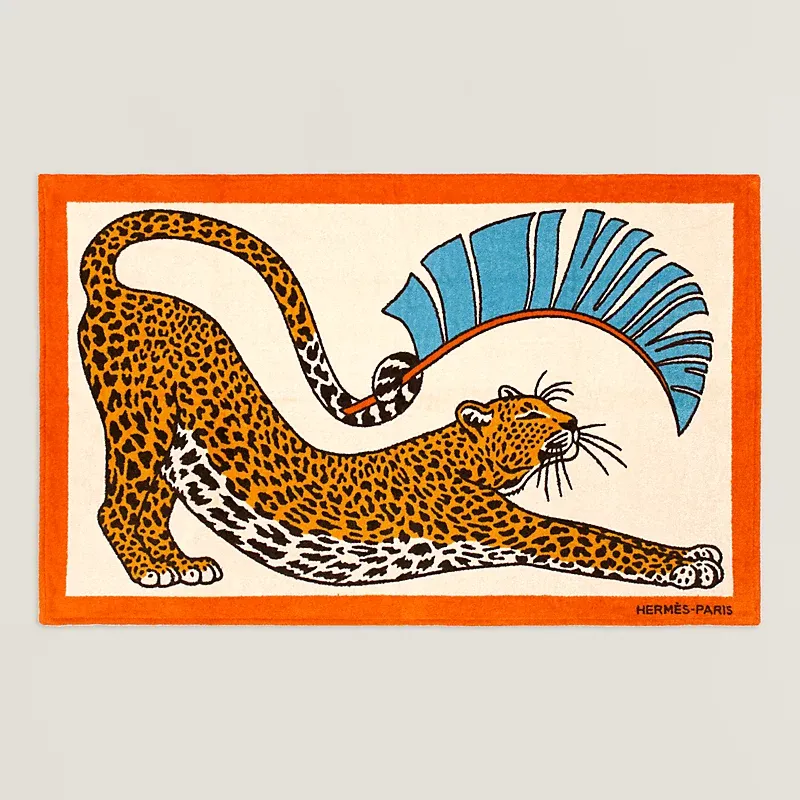 Rectangular rug with an orange border, showing a stretching leopard motif and a blue abstract fan, Hermès Paris in the corner.