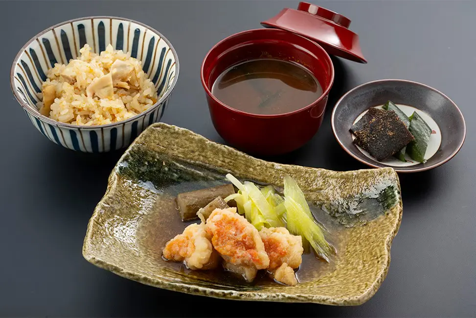 Japanese meal set with a triangular ceramic plate of fried shrimp and vegetables, a bowl of rice, miso soup, and a small side dish on a dark table.