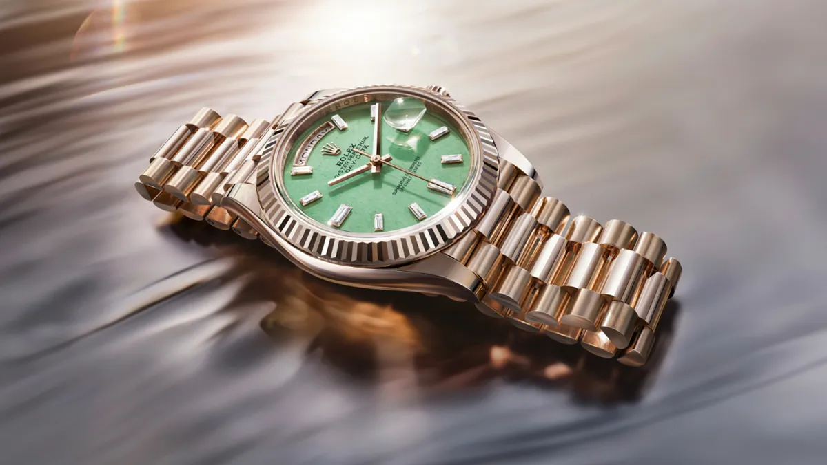 Rose-gold Rolex watch with a green dial, diamond markers, and a fluted bezel on a reflective surface.