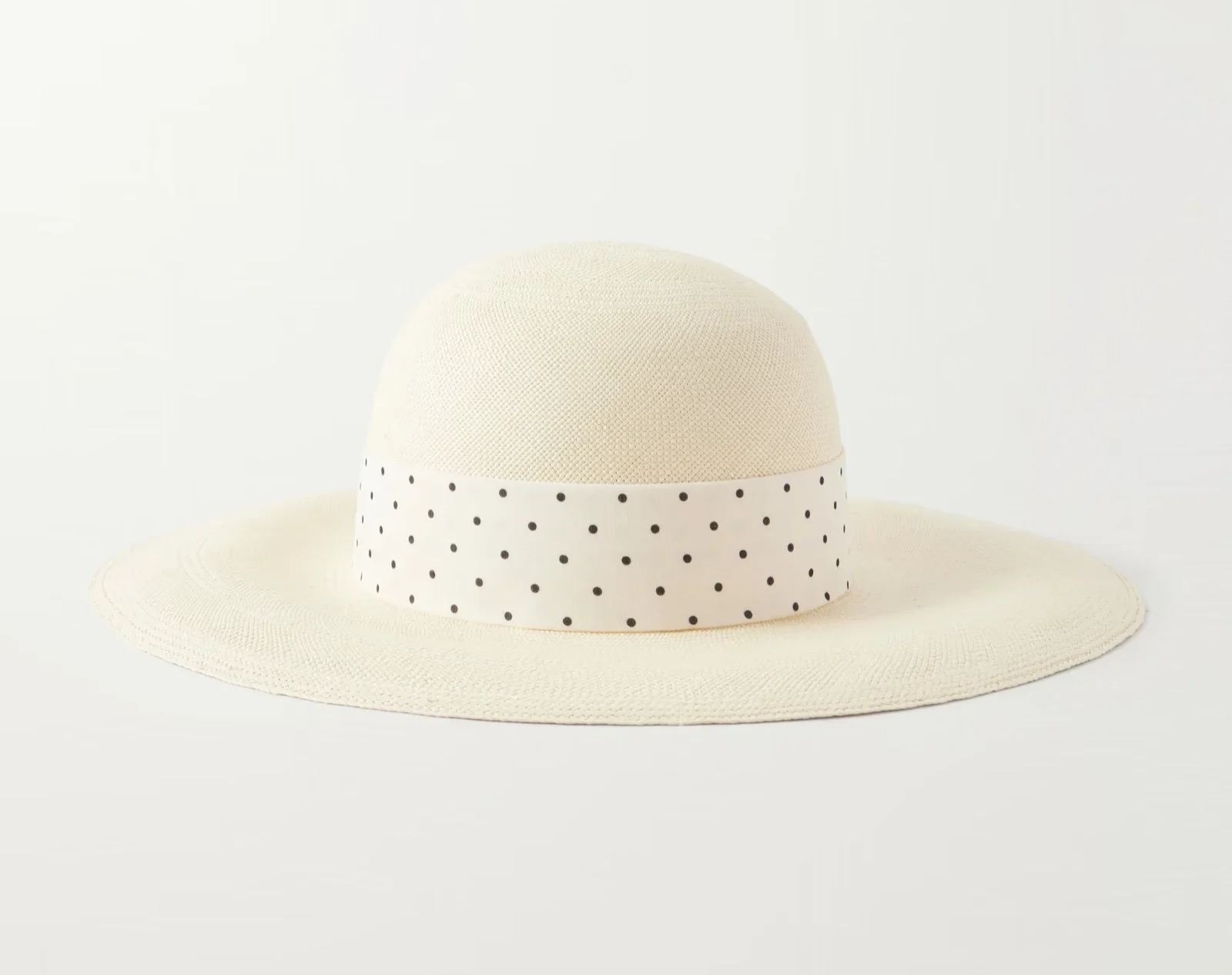 Beige straw sun hat with a white ribbon featuring black polka dots, placed on a light background.